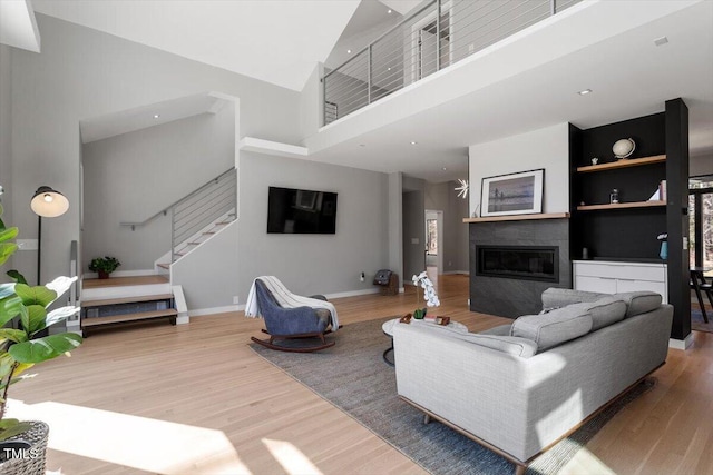 living room with a glass covered fireplace, a high ceiling, wood finished floors, and stairs