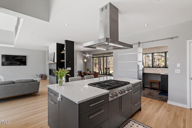 kitchen featuring a kitchen island, light wood-style flooring, stainless steel gas stovetop, open floor plan, and island range hood