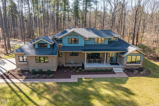 view of front facade with a front yard, brick siding, covered porch, and a shingled roof