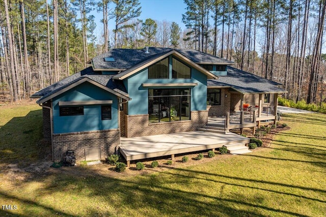 rear view of house featuring a yard, a view of trees, brick siding, and a wooden deck