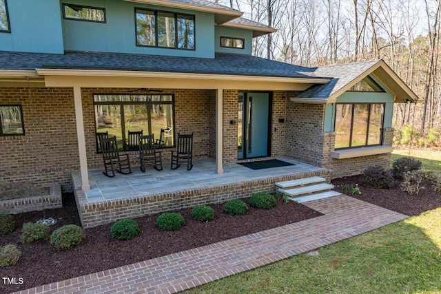 entrance to property with a patio area, brick siding, and roof with shingles