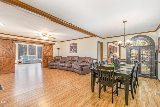 dining space with a barn door, a textured ceiling, crown molding, and light wood-style floors
