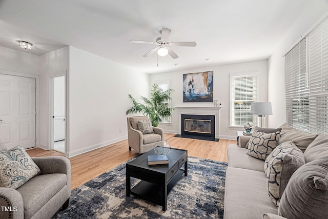 living area with a fireplace with flush hearth, ceiling fan, baseboards, and wood finished floors