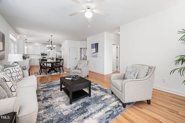 living area featuring ceiling fan with notable chandelier, baseboards, and light wood-type flooring