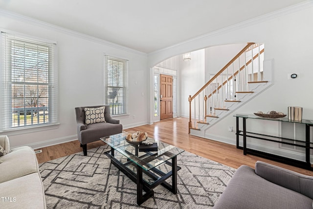 living room featuring wood finished floors, stairway, arched walkways, and ornamental molding