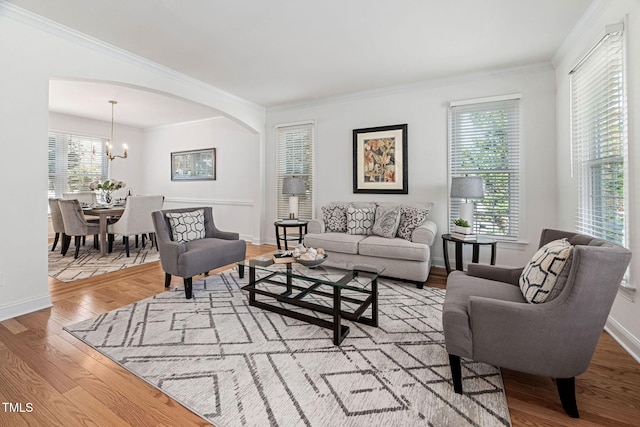 living room featuring arched walkways, an inviting chandelier, wood finished floors, and ornamental molding