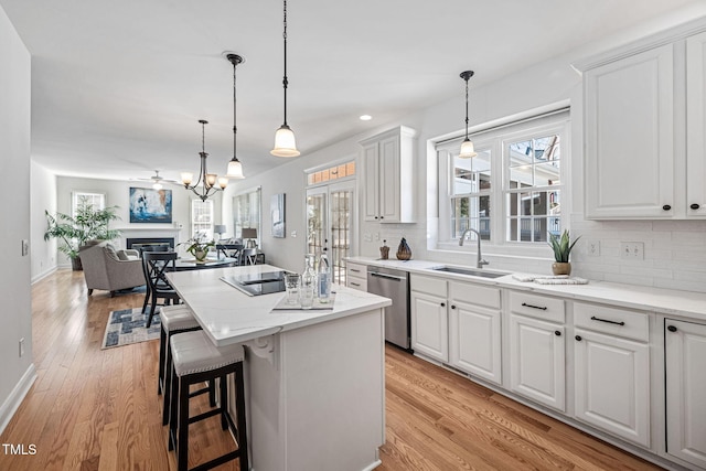 kitchen featuring a sink, open floor plan, light wood-style floors, a glass covered fireplace, and stainless steel dishwasher