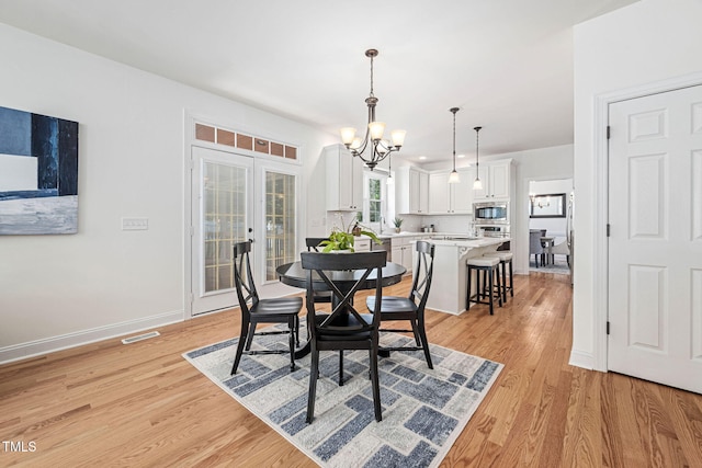 dining room featuring visible vents, baseboards, a chandelier, french doors, and light wood-style floors