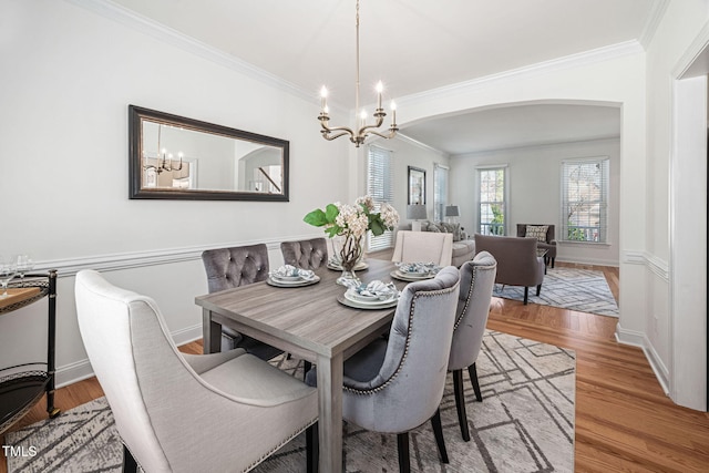 dining room featuring arched walkways, a notable chandelier, wood finished floors, and ornamental molding