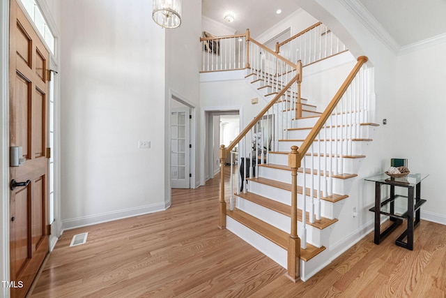 foyer with baseboards, visible vents, arched walkways, light wood-style floors, and crown molding