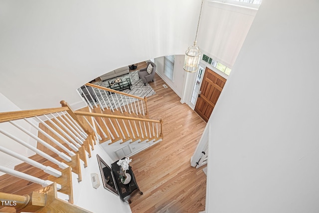 staircase with an inviting chandelier, wood finished floors, visible vents, and a towering ceiling