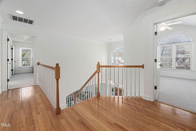 hallway with visible vents, an upstairs landing, wood-type flooring, and ornamental molding