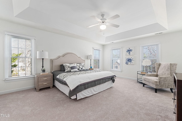 bedroom with a tray ceiling, multiple windows, light carpet, and visible vents