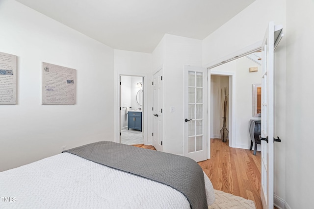 bedroom featuring light wood-style floors, baseboards, french doors, and connected bathroom