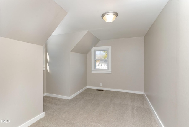 additional living space featuring baseboards, lofted ceiling, visible vents, and light colored carpet