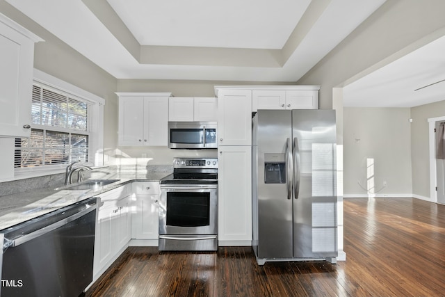 kitchen with white cabinets, dark wood-type flooring, light stone countertops, stainless steel appliances, and a sink