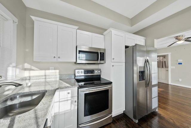 kitchen featuring stainless steel appliances, dark wood-style flooring, a sink, white cabinets, and light stone countertops