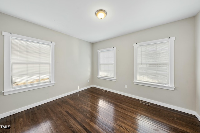 empty room with hardwood / wood-style flooring, visible vents, and baseboards