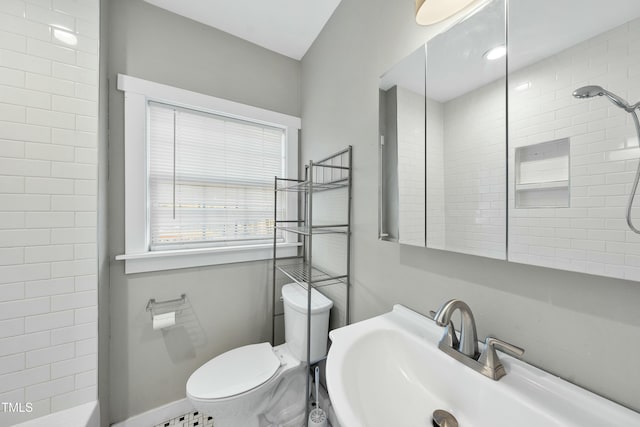 bathroom with baseboards, tiled shower, a sink, and toilet