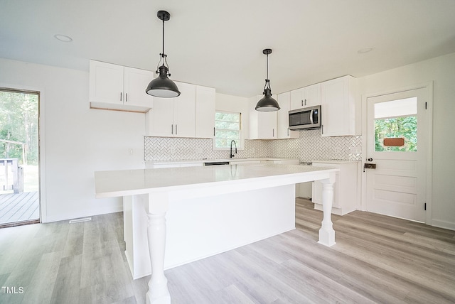 kitchen with light wood finished floors, stainless steel microwave, a sink, and backsplash