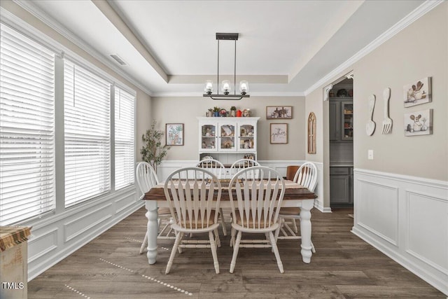 dining space featuring a chandelier, a decorative wall, dark wood finished floors, and a tray ceiling