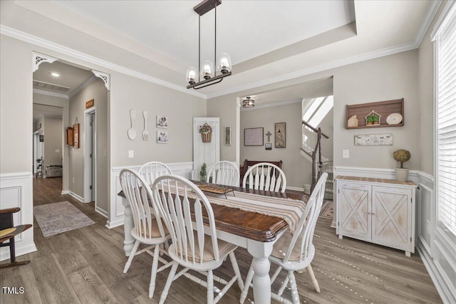 dining area featuring a wainscoted wall, wood finished floors, crown molding, a raised ceiling, and a chandelier