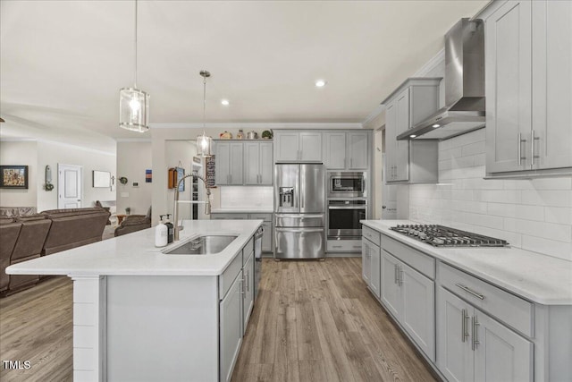 kitchen with open floor plan, gray cabinets, appliances with stainless steel finishes, wall chimney exhaust hood, and a sink