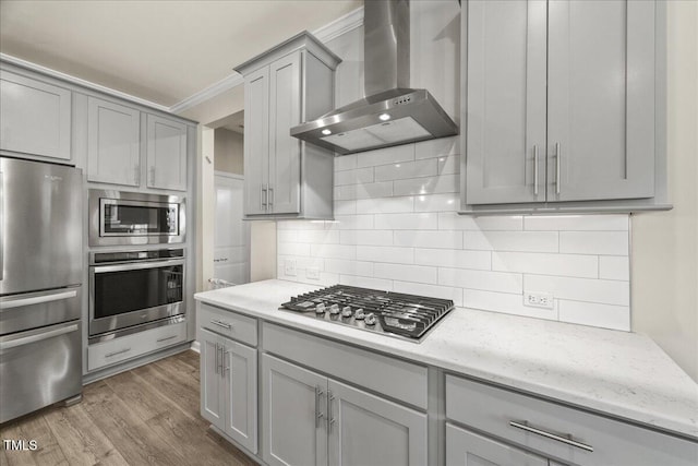 kitchen featuring gray cabinetry, tasteful backsplash, wood finished floors, appliances with stainless steel finishes, and wall chimney exhaust hood