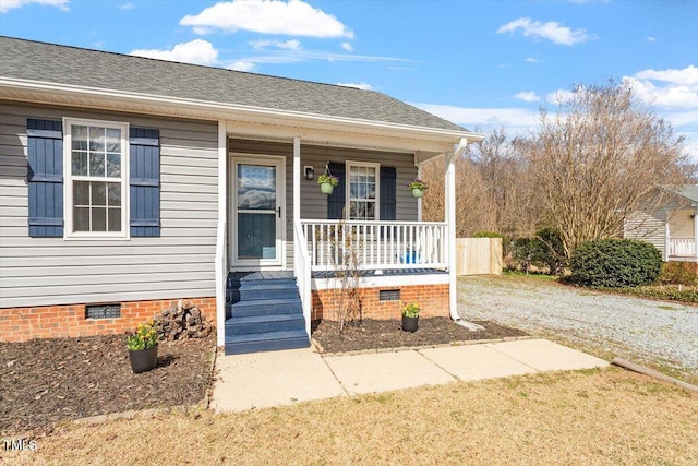 view of exterior entry with a porch, crawl space, roof with shingles, and gravel driveway