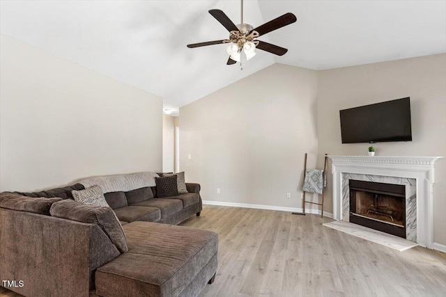 living area with a fireplace, light wood finished floors, vaulted ceiling, ceiling fan, and baseboards