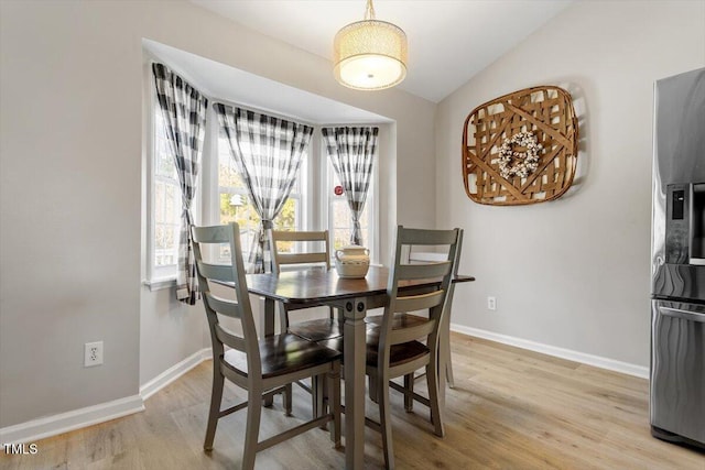 dining space featuring lofted ceiling, light wood finished floors, and baseboards