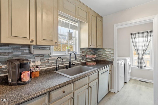 kitchen with visible vents, dark countertops, washing machine and clothes dryer, white dishwasher, and a sink