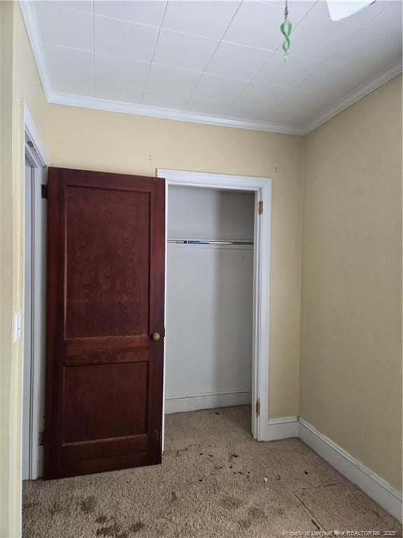 unfurnished bedroom featuring ornamental molding, carpet, a closet, and baseboards