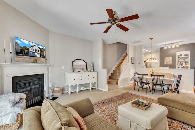 carpeted living room featuring baseboards, stairway, a ceiling fan, and a glass covered fireplace