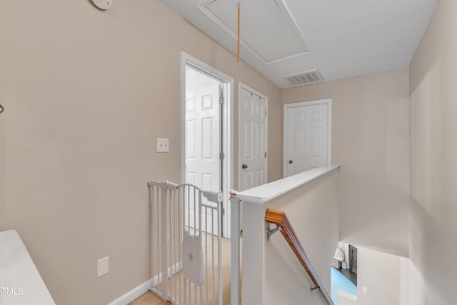 hall featuring attic access, visible vents, baseboards, and an upstairs landing