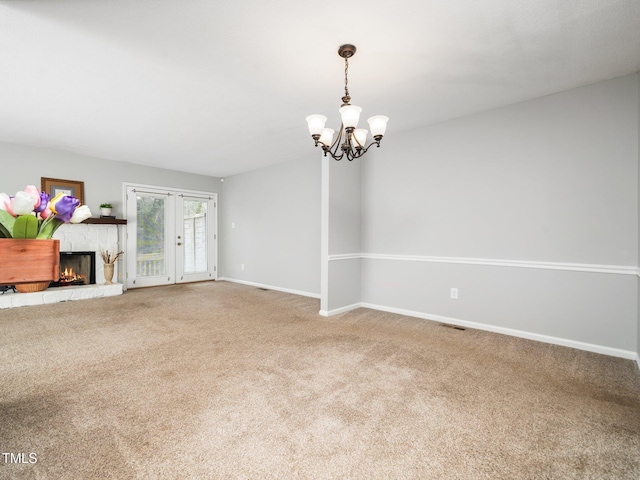 unfurnished living room with carpet, a fireplace, an inviting chandelier, and baseboards