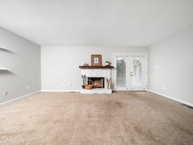 unfurnished living room featuring baseboards, french doors, a textured ceiling, a stone fireplace, and carpet flooring