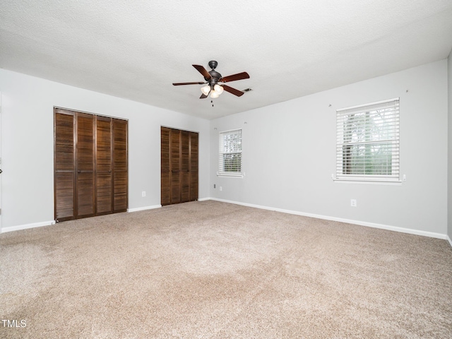 unfurnished bedroom with multiple windows, a textured ceiling, carpet flooring, and two closets