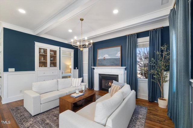 living area featuring dark wood-style flooring, a lit fireplace, ornamental molding, wainscoting, and beamed ceiling