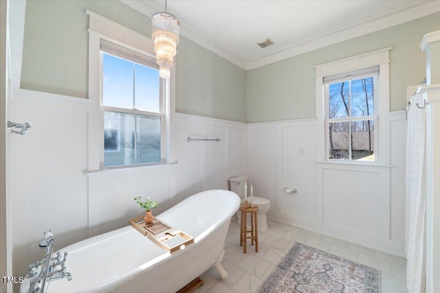 full bath featuring a freestanding tub, toilet, a decorative wall, a wainscoted wall, and visible vents