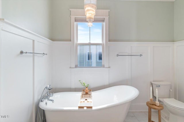 full bath featuring toilet, a soaking tub, a decorative wall, and a wainscoted wall