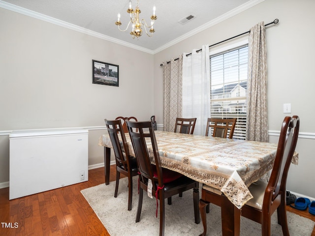 dining space featuring baseboards, visible vents, ornamental molding, wood finished floors, and a notable chandelier