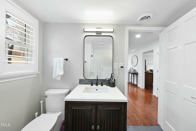 half bath featuring visible vents, toilet, wood finished floors, and vanity