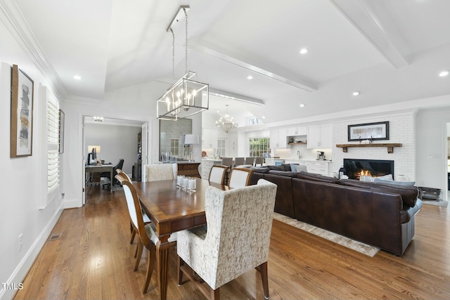 dining area with vaulted ceiling with beams, baseboards, a fireplace, wood finished floors, and a notable chandelier