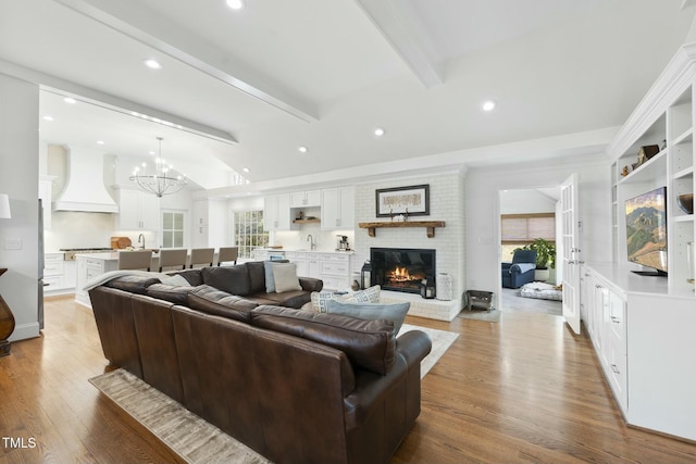 living room with wood finished floors, lofted ceiling with beams, recessed lighting, a brick fireplace, and a notable chandelier