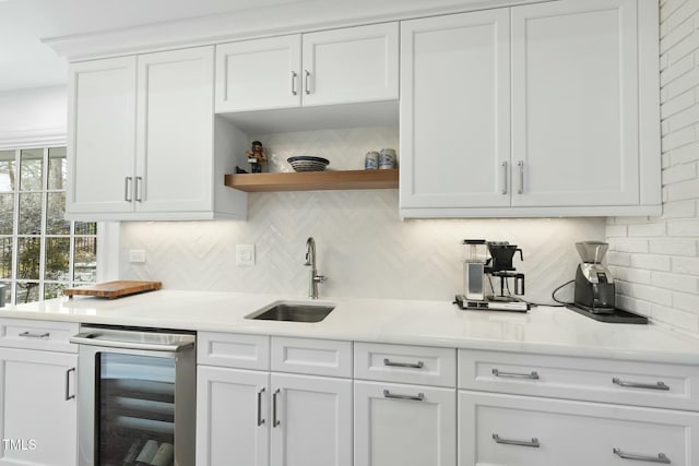 kitchen with wine cooler, white cabinetry, light countertops, and a sink