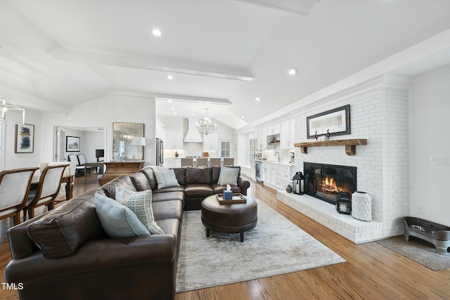 living room with an inviting chandelier, recessed lighting, vaulted ceiling, light wood-style floors, and a brick fireplace