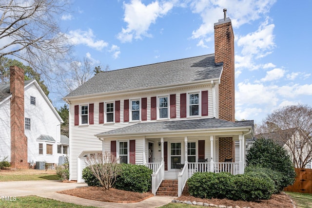 view of front of home with covered porch, concrete driveway, a shingled roof, and a chimney