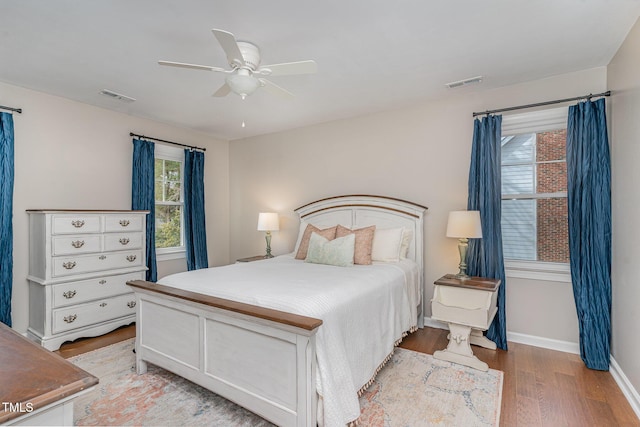 bedroom featuring light wood-style flooring, a ceiling fan, visible vents, and baseboards