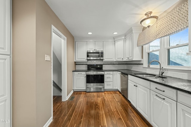 kitchen with stainless steel appliances, dark wood-type flooring, a sink, white cabinetry, and tasteful backsplash